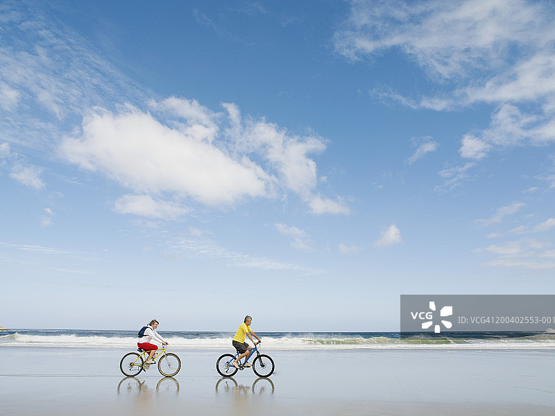 一对成熟的夫妇在海滩上骑自行车，侧视图图片素材