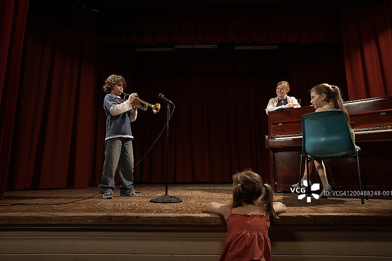 男孩(10-12)在舞台上吹小号，由老师和两个女孩观看图片素材