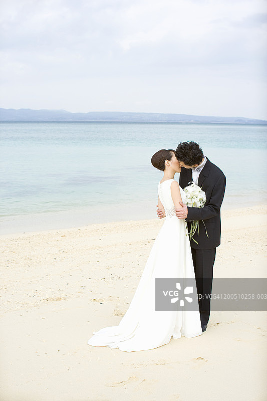 新娘和新郎在沙滩上接吻，侧视图图片素材