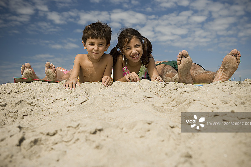 男孩和女孩(4-10)躺在父母的两脚之间的海滩，肖像图片素材