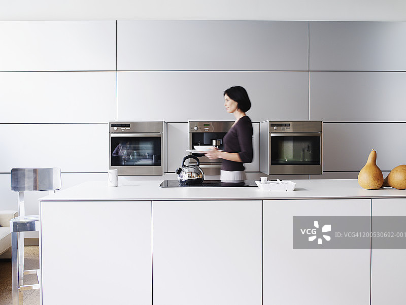 在家庭厨房里，女人扛着餐具，侧视图图片素材