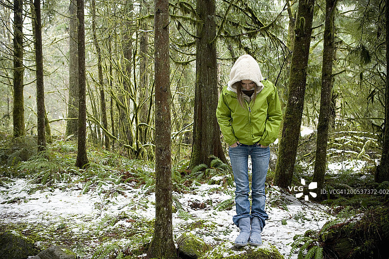 少女(14-16岁)站在白雪覆盖的森林里，向下看图片素材