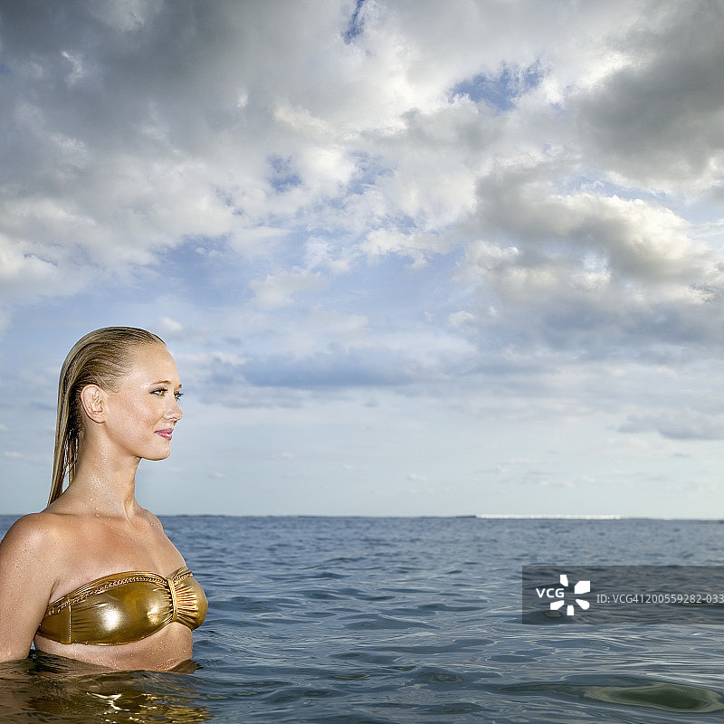 年轻女子站在水里，望着别处，微笑着，侧视图片素材