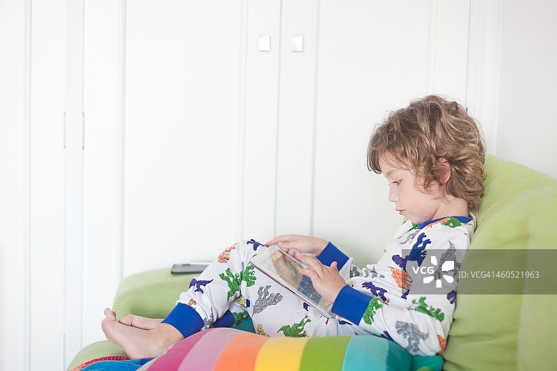 金发男孩穿着睡衣玩平板电脑图片素材