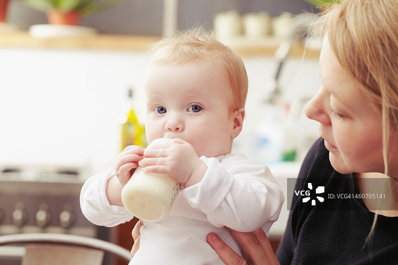 母亲和婴儿带着奶瓶坐在厨房里图片素材