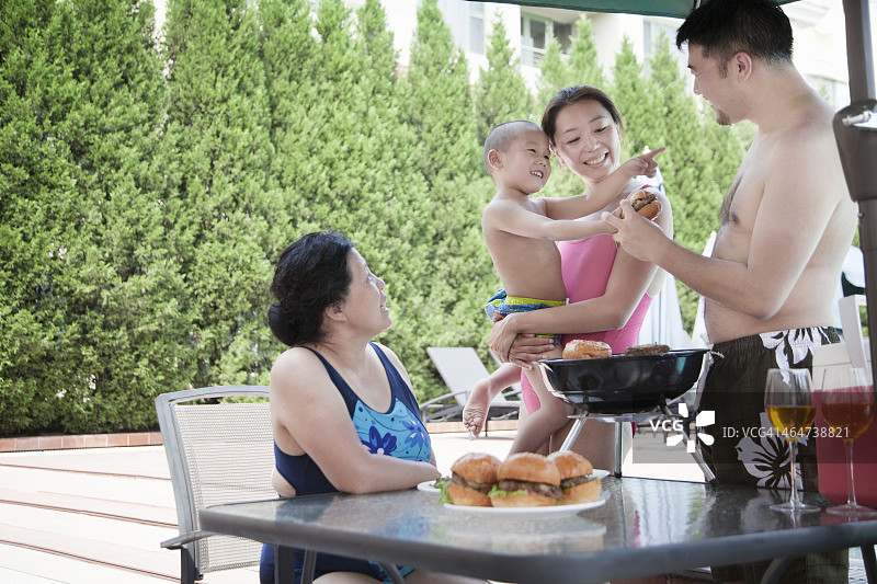 微笑的多代家庭烧烤在游泳池度假图片素材