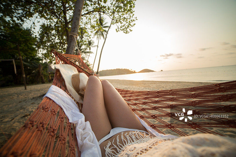 在异国情调的海滩上，一个女人在吊床上看日落图片素材