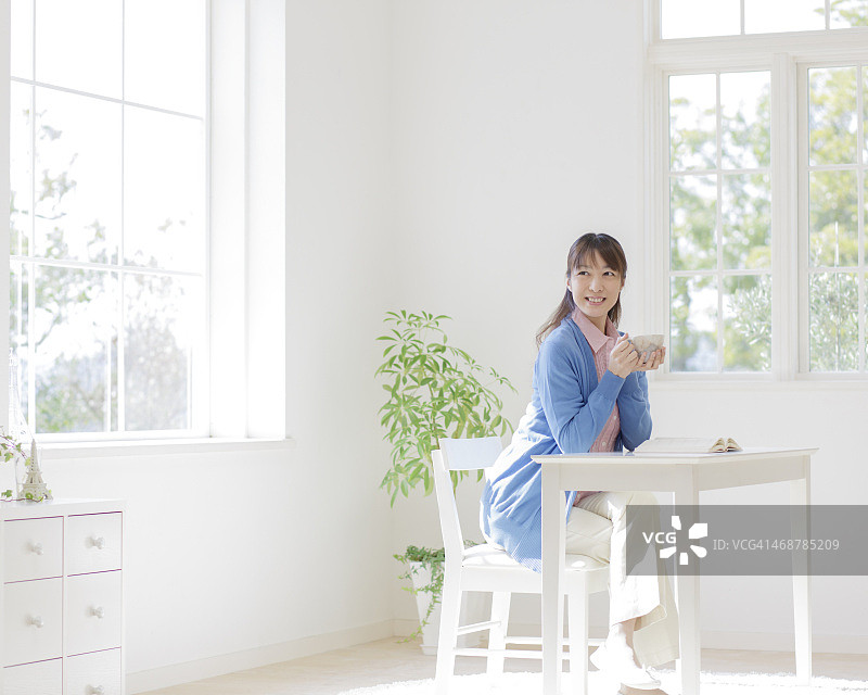 年轻女子坐在白色的房间里喝茶图片素材