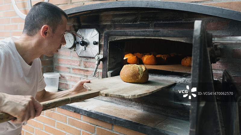面包师在传统的炉子里检查面包。图片素材