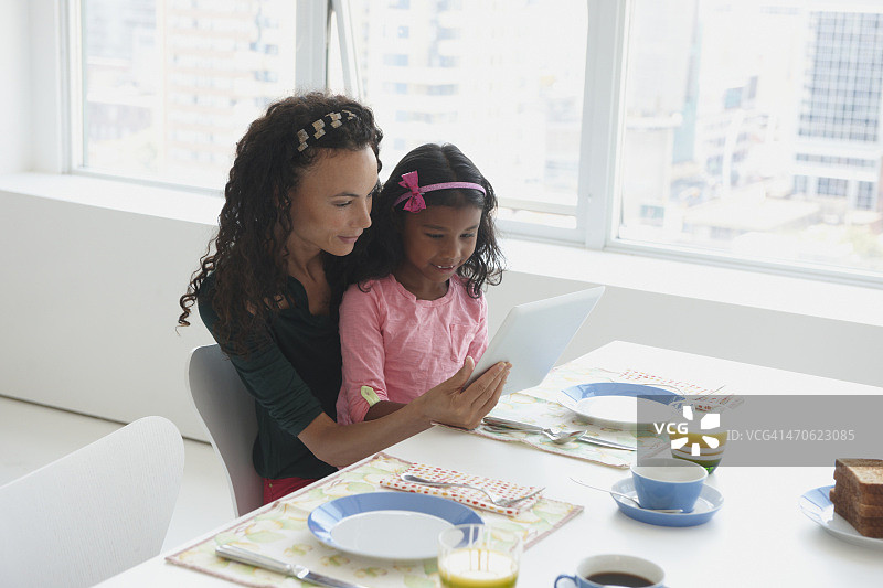 母亲和女儿在餐桌上使用电子平板电脑图片素材