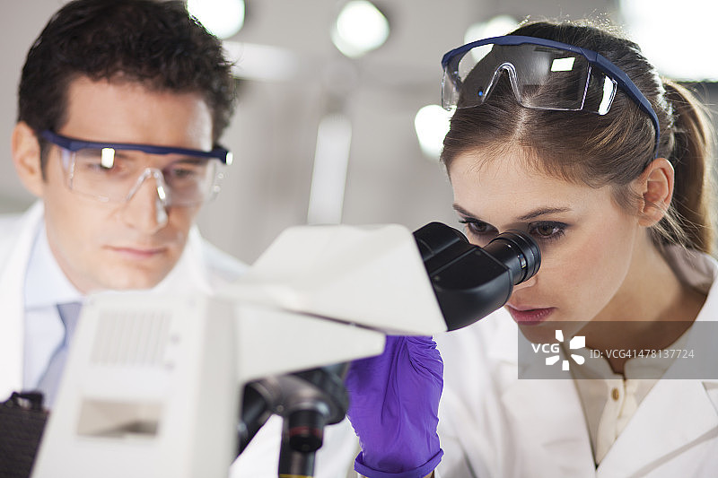 两个科学家在实验室里通过显微镜观察图片素材