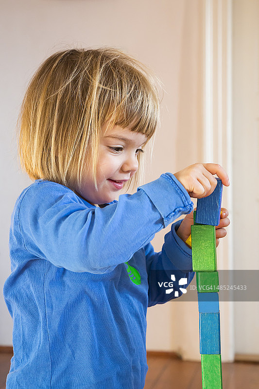 小女孩玩着蓝色和绿色的木制建筑砖图片素材