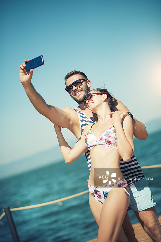 一对迷人的微笑情侣在海边用智能手机自拍图片素材