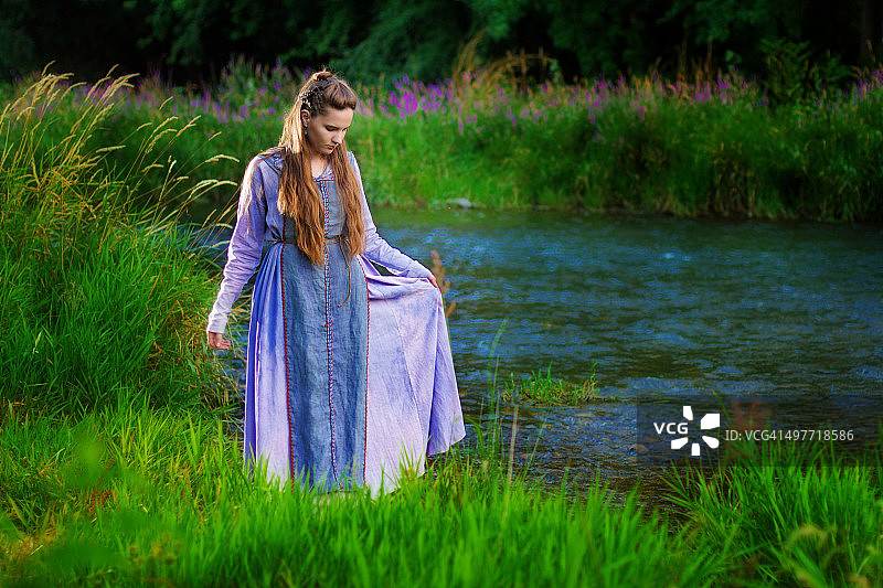 黄昏时分，身着维京服饰的年轻女子挽着裙摆站在河边图片素材