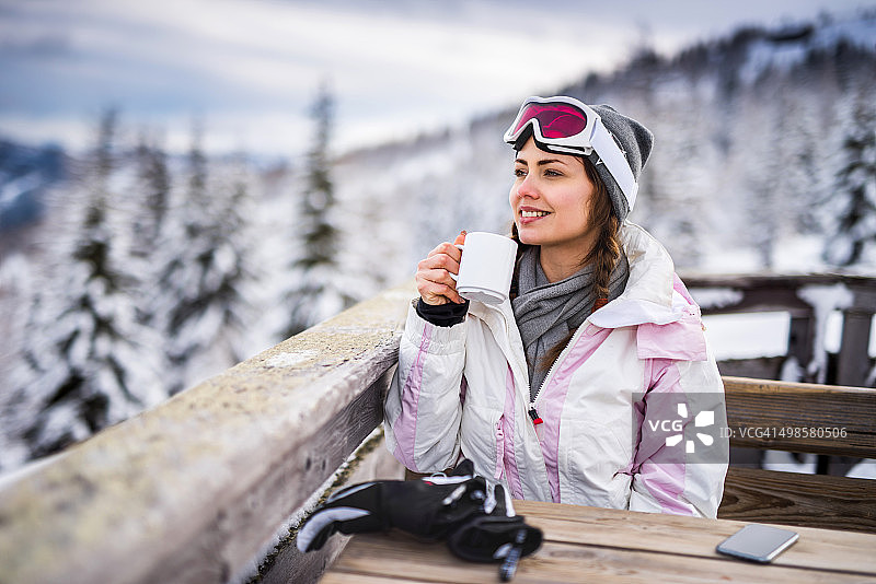 年轻微笑的女人放松在一个咖啡馆在滑雪胜地。图片素材