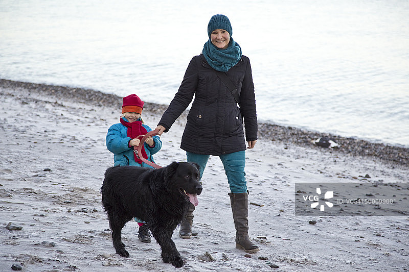 德国，石勒苏益格-荷尔斯泰因州，基尔，母女带着拉布拉多犬沿着海滩散步图片素材