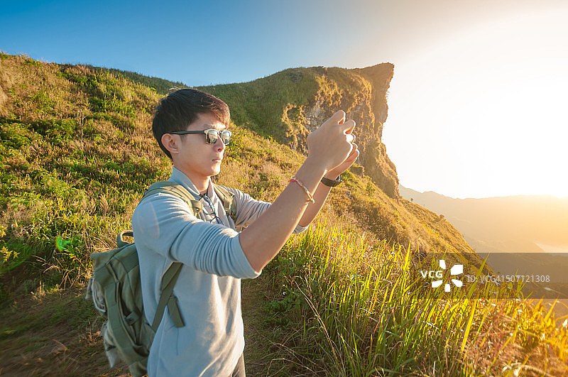 年轻的旅行者站在山上望着夕阳。图片素材