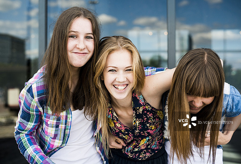 三个年轻女子在玻璃办公楼前大笑的肖像图片素材