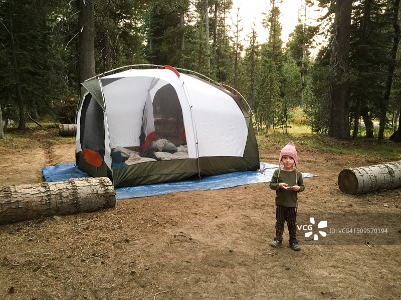 在加州内华达山脉的林地露营地，一个蹒跚学步的小女孩在她的家庭帐篷旁图片素材