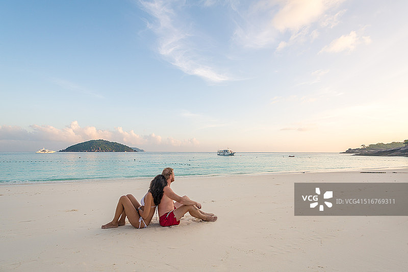 一对成年夫妇背靠背坐在海滩上图片素材