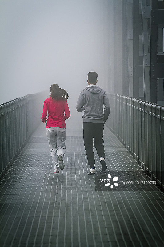 一对情侣在铁桥上的雾中奔跑图片素材