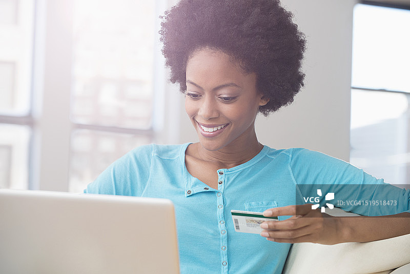 一位非裔美国妇女在沙发上用信用卡在笔记本电脑上购物图片素材