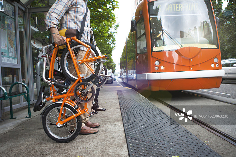 一名男子骑着折叠自行车在城市周围等待电车图片素材