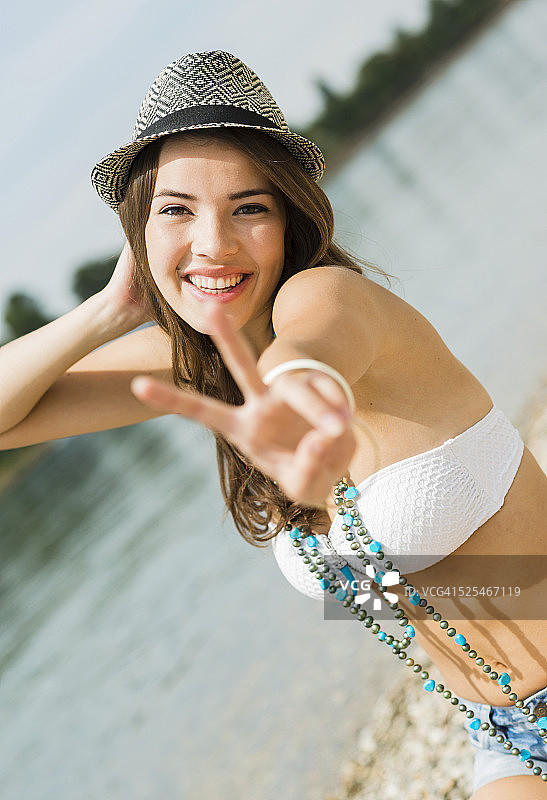在海滩上微笑的年轻女子展示胜利标志的肖像图片素材