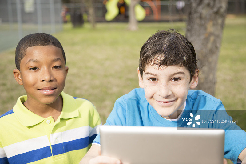 科技:两个男孩在公园和学校里享受户外平板电脑。图片素材