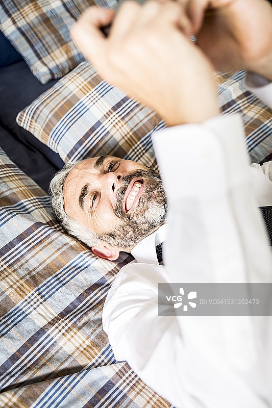 一个快乐的商人躺在床上看他的智能手机图片素材