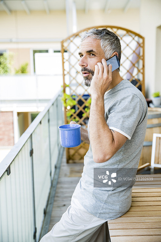 男人在阳台上拿着一杯咖啡用智能手机打电话图片素材