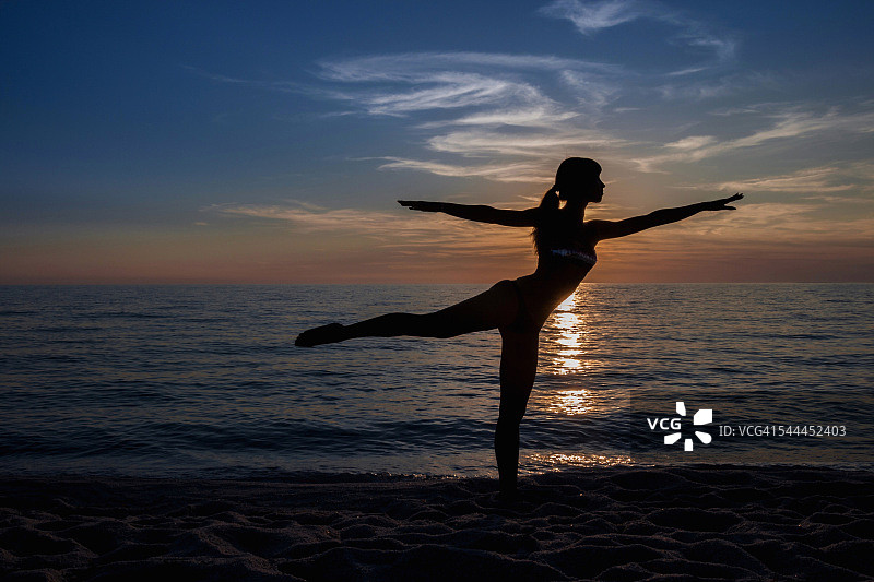 年轻女子的剪影练习瑜伽姿势在海滩上日落，奥里斯塔诺，撒丁岛，意大利图片素材
