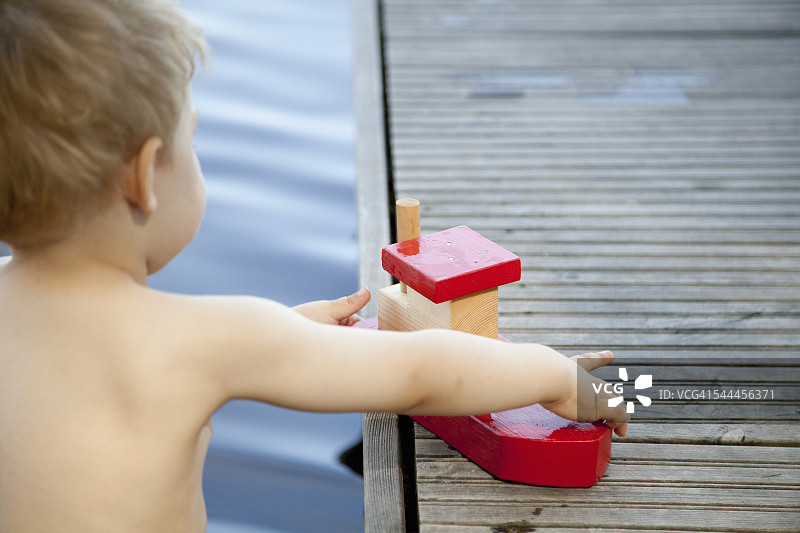男子蹒跚学步玩玩具船在码头的后视图图片素材