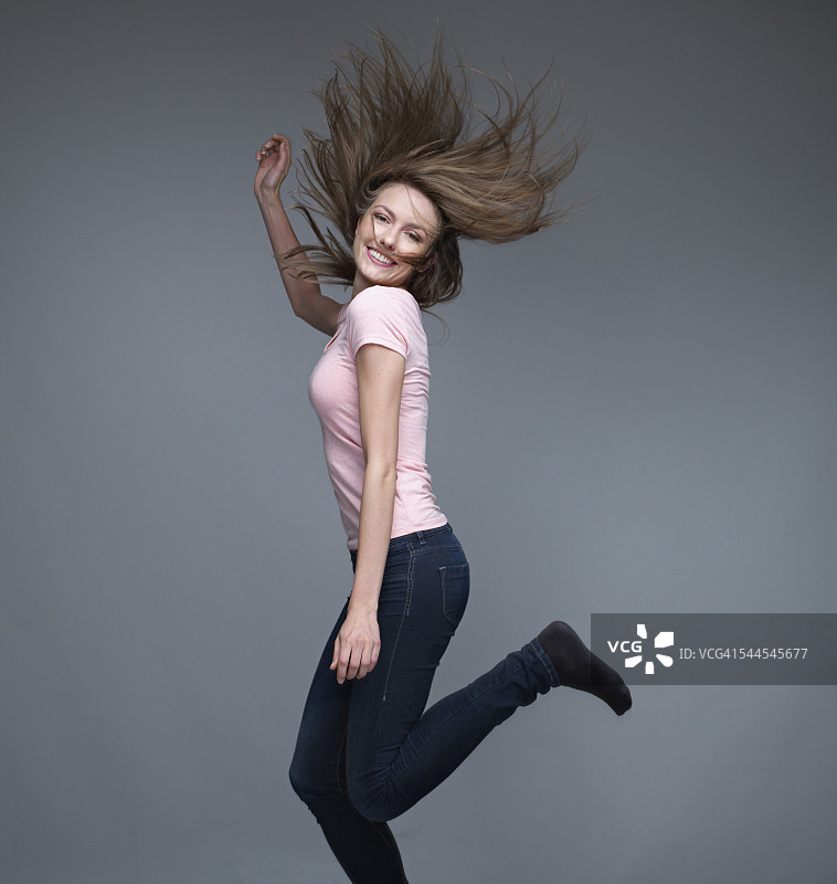 微笑的年轻女子在灰色背景前跳舞的肖像图片素材