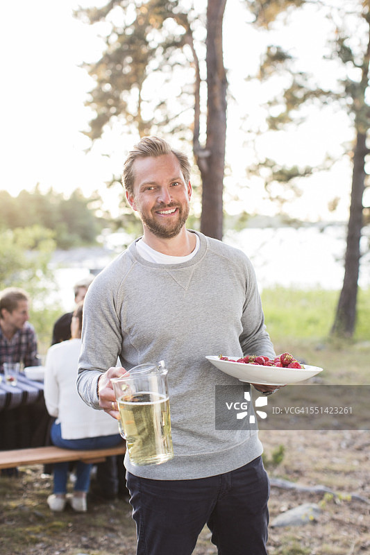 肖像快乐的人拿着啤酒壶和草莓和朋友坐在野餐桌上的背景图片素材