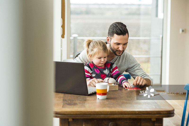 父亲和女儿与笔记本电脑和游戏在木桌图片素材