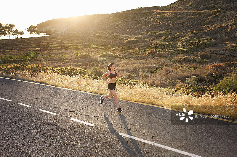 日落时分，女人在狂野的道路上慢跑图片素材