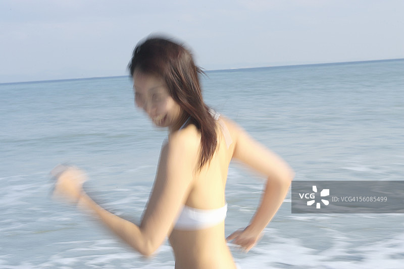 一个穿着比基尼的年轻女子在海滩上跑步，动作模糊图片素材