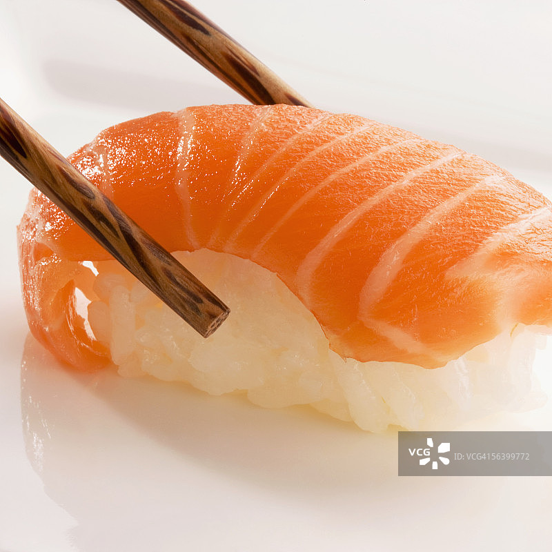 手握寿司与三文鱼夹在筷子之间的特写图片素材