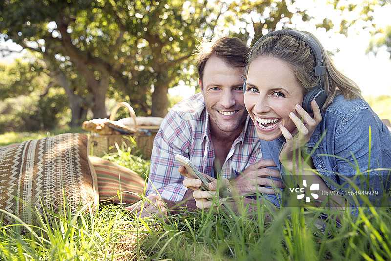 一对幸福的夫妇躺在草地上，女人在用智能手机听音乐图片素材