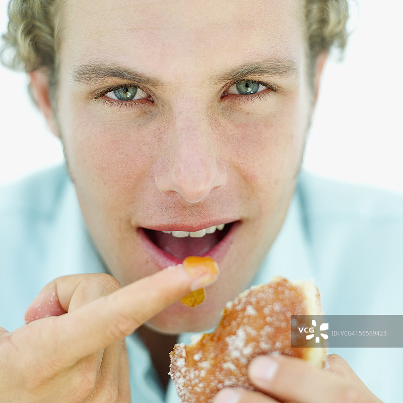 一个年轻男子舔甜甜圈的馅的特写图片素材