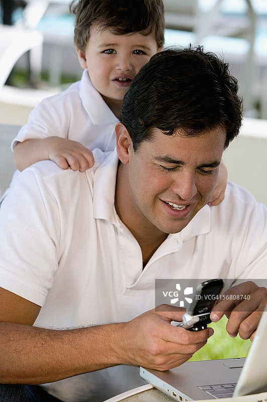 一个父亲使用手机的特写镜头，他的儿子站在他身后图片素材