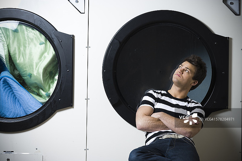 男人坐在洗衣店双臂交叉看着烘干机图片素材