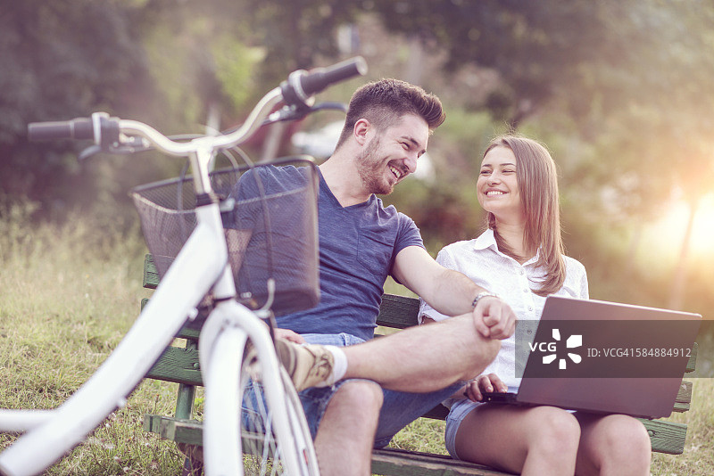 微笑的夫妇坐在长椅上，骑完自行车后使用笔记本电脑图片素材