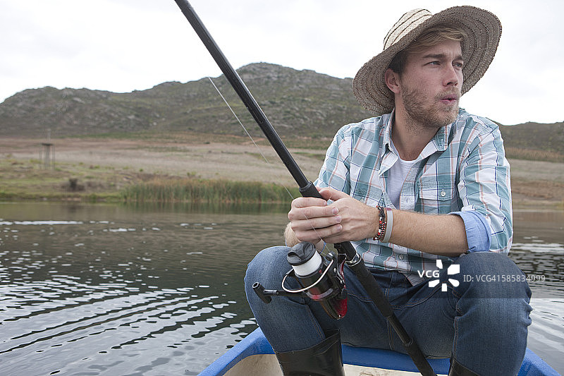 钓鱼的年轻人坐在湖上的独木舟上图片素材