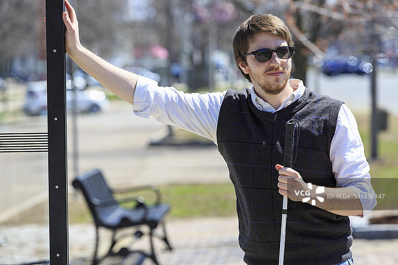 一个年轻的盲人拄着拐杖在公共汽车站等车图片素材
