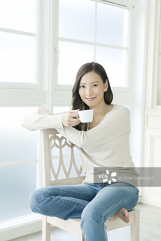 一个年轻女人拿着咖啡杯坐在椅子上图片素材