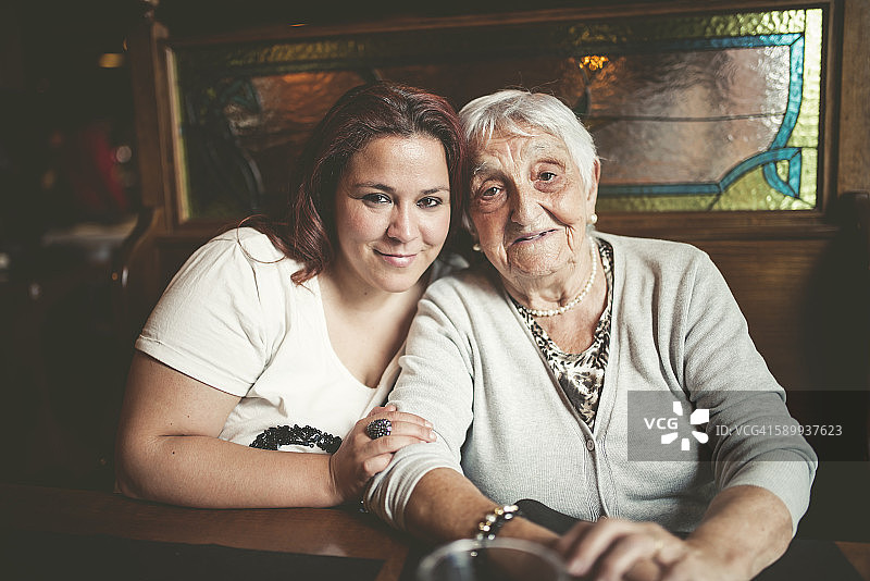 一位微笑的老妇人和她的孙女在一家餐馆里面对面坐着图片素材