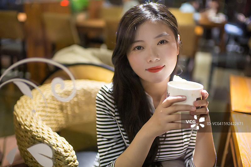 年轻的亚洲女人在咖啡馆的窗口喝咖啡图片素材