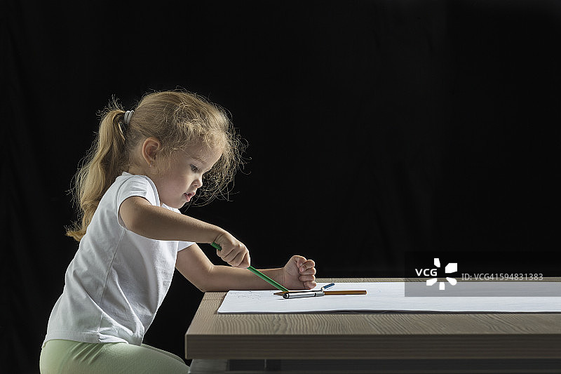 侧面的女孩在纸上画在桌子上的黑色背景图片素材